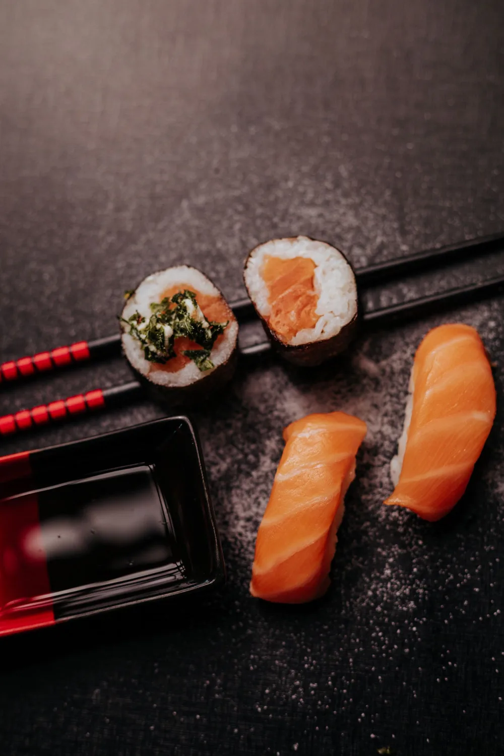 Lachs-Sushi mit Essstäbchen auf einer dunklen Oberfläche